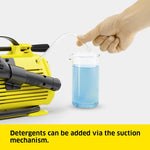 Load image into Gallery viewer, Yellow pressure washer with a hand adding blue detergent from a measuring cup.