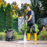 Load image into Gallery viewer, A man in a backyard is pressure-washing a stone patio with a black and gray portable pressure washer. The pressure washer is positioned to the left of the man on the wet stone surface.