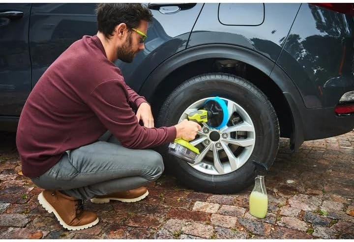Man changing a tire on a car with tools and a bottle of juice on the ground.