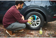 Man changing a tire on a car with tools and a bottle of juice on the ground.