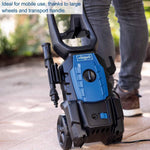 Load image into Gallery viewer, Schoppel high-pressure water cleaner in blue and black, shown being used outdoors with a person's legs visible in the background.