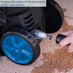 Load image into Gallery viewer, Close-up of a black garden hose system with a blue wheel, showing a clear click-clamp connector attached, with a hand holding a black hose nozzle on a gravel surface. A text box in the top left reads: 'Practical click system for all conventional garden hose systems.