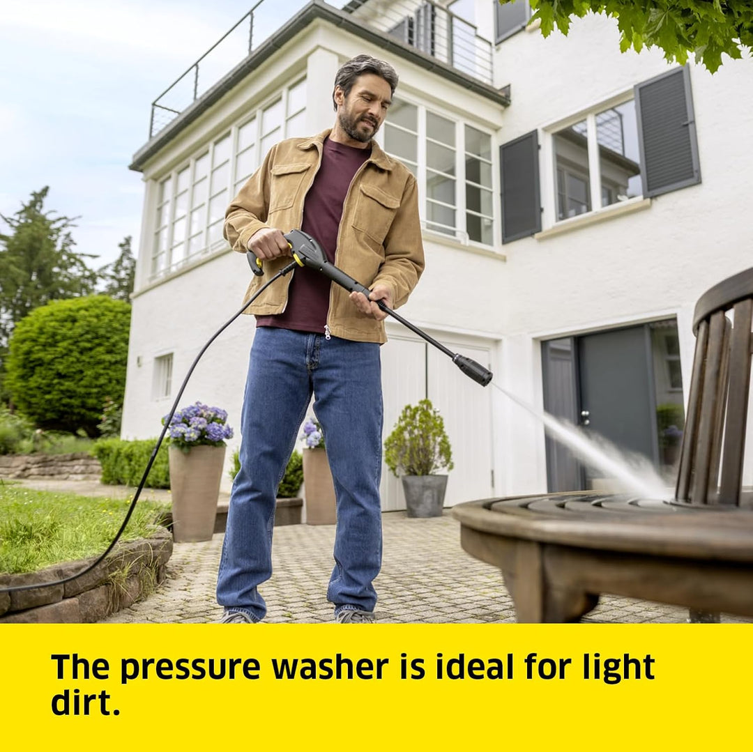 Man using a pressure washer to clean outdoor furniture in front of a house.