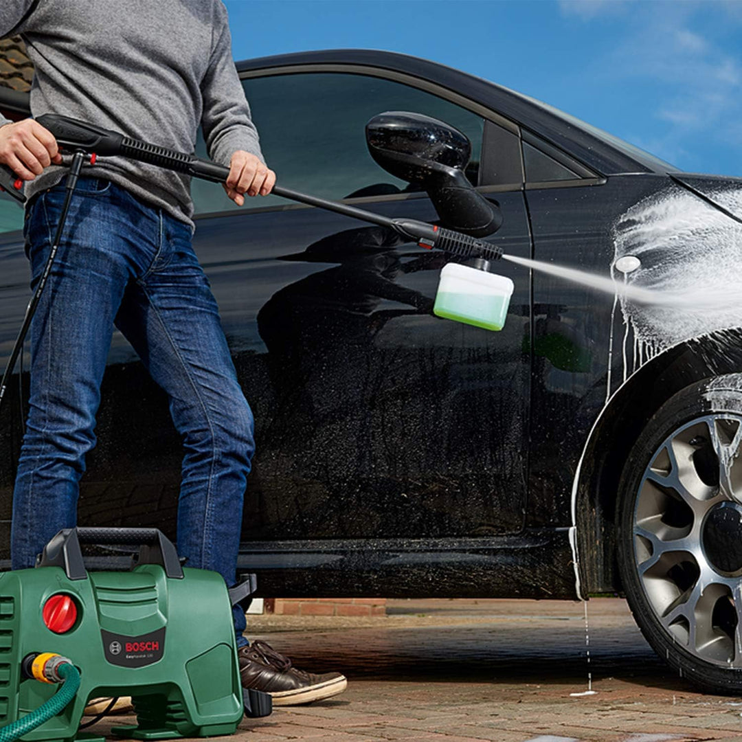 Person using a pressure washer to clean a black car on a sunny day.