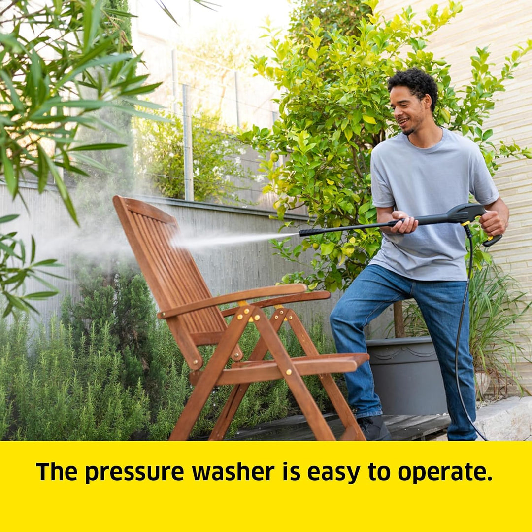 A man in a backyard is using a pressure washer on a wooden folding chair, with green plants and a house wall in the background. A yellow text banner at the bottom reads, 'The pressure washer is easy to operate.